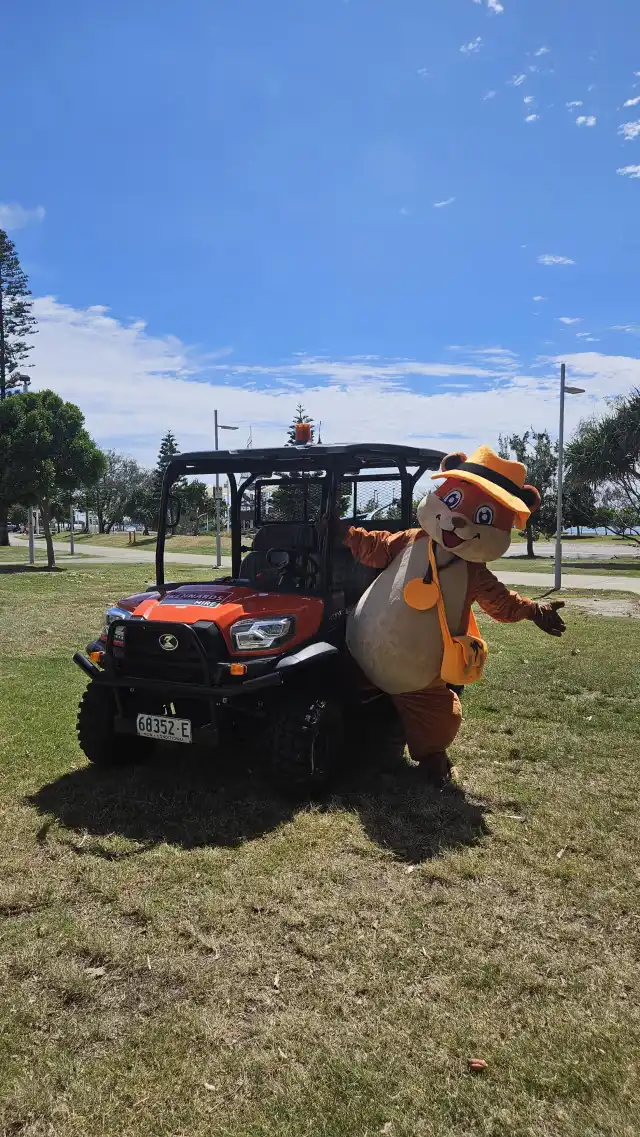 Sunny the Quokka mascot standing by an orange utility vehicle at Broadwater Parklands, Gold Coast. A fun representation of the Sunny Link™ premium souvenir apparel brand.