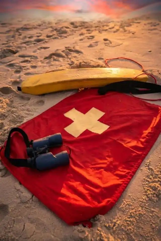 A close-up of a rescue flotation device and binoculars on the sand, representing the emergency equipment funded by Sunny merch for our volunteer responder network.